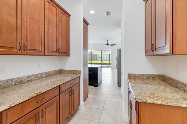 kitchen featuring light stone counters, brown cabinets, ceiling fan, and light tile patterned flooring