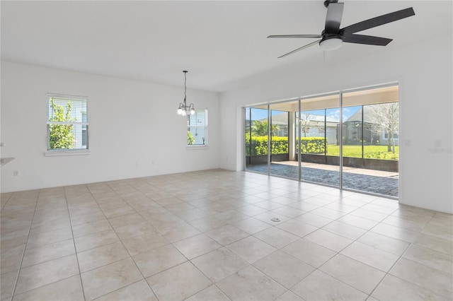 empty room with a wealth of natural light, light tile patterned flooring, and ceiling fan with notable chandelier