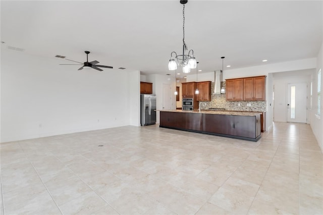 kitchen with wall chimney exhaust hood, open floor plan, decorative light fixtures, stainless steel appliances, and backsplash