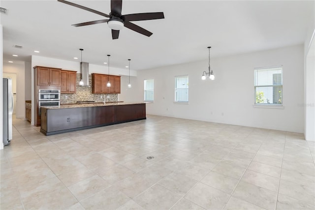 kitchen featuring stainless steel appliances, visible vents, wall chimney range hood, decorative backsplash, and brown cabinets