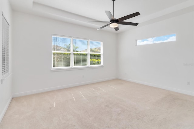 unfurnished room featuring baseboards, ceiling fan, a tray ceiling, and light colored carpet