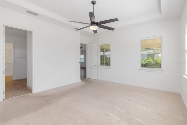 unfurnished bedroom with carpet floors, a tray ceiling, multiple windows, and visible vents