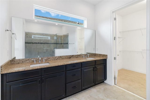 bathroom featuring a tile shower, double vanity, a sink, and a walk in closet