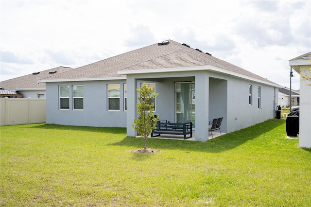 rear view of property with a patio, a shingled roof, fence, a lawn, and stucco siding