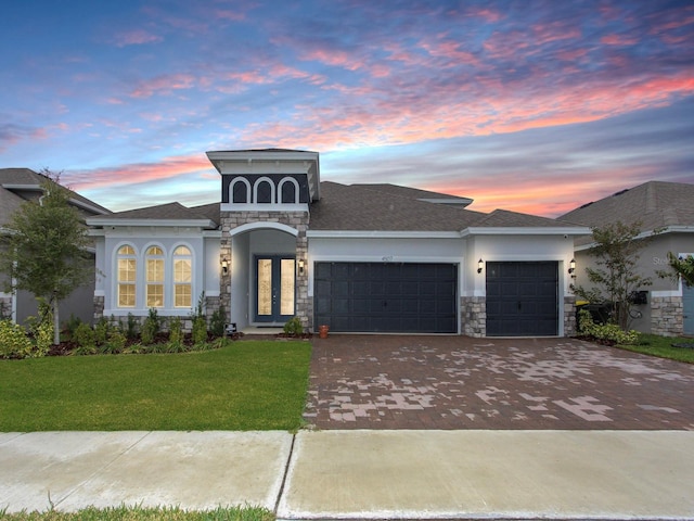 view of front of home with stone siding, an attached garage, decorative driveway, french doors, and stucco siding