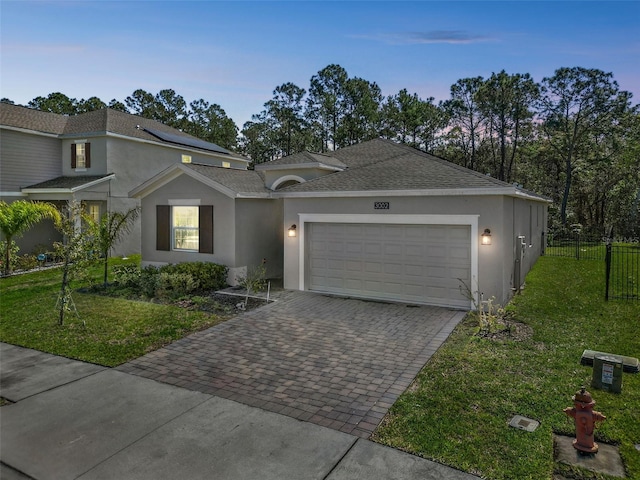 view of front facade featuring decorative driveway, stucco siding, an attached garage, fence, and a front lawn