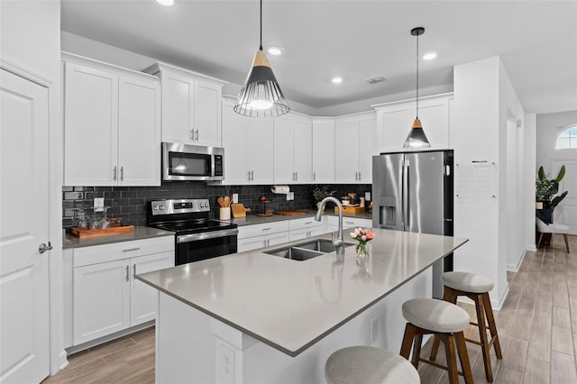 kitchen featuring a breakfast bar, wood finish floors, a sink, appliances with stainless steel finishes, and decorative backsplash