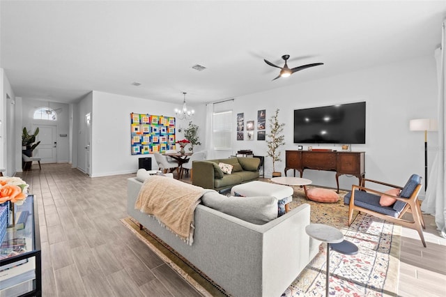 living room with light wood-style floors, baseboards, visible vents, and ceiling fan with notable chandelier