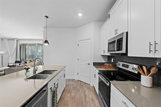 kitchen featuring light wood finished floors, decorative backsplash, stainless steel appliances, white cabinetry, and a sink