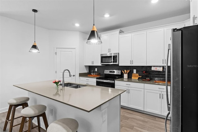 kitchen with white cabinets, decorative backsplash, light wood-style flooring, appliances with stainless steel finishes, and a sink