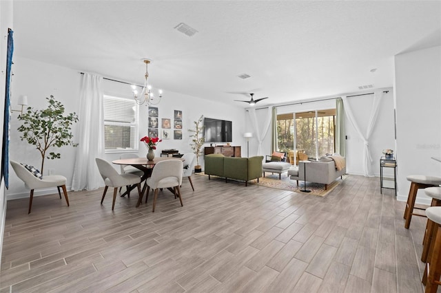 dining room featuring light wood finished floors, visible vents, a textured ceiling, and ceiling fan with notable chandelier