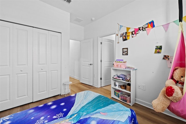 bedroom with a closet, wood finished floors, visible vents, and baseboards