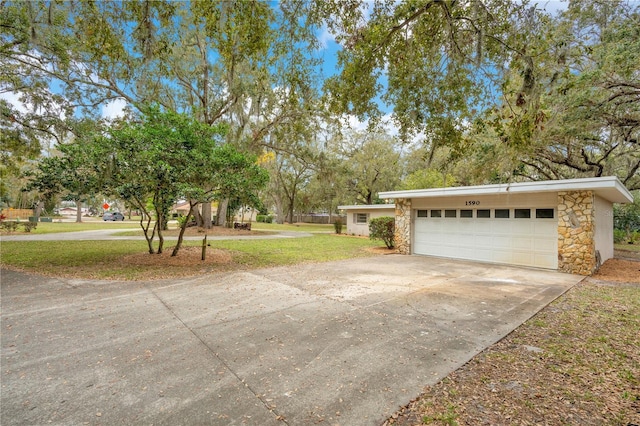 exterior space with a garage, stone siding, concrete driveway, and a yard