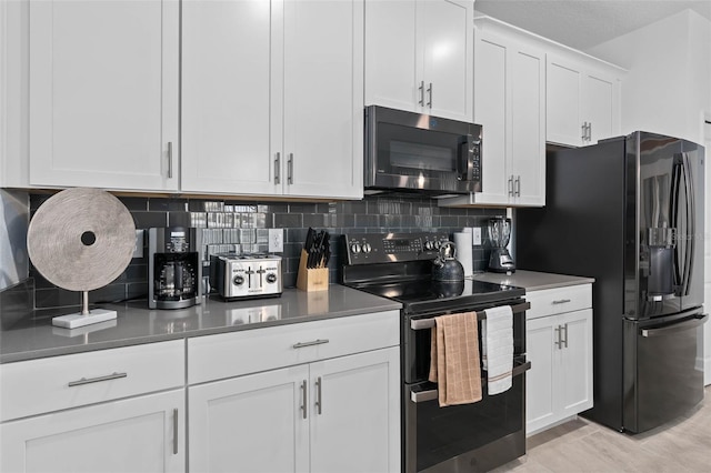 kitchen featuring white cabinetry, black appliances, light wood-type flooring, and backsplash