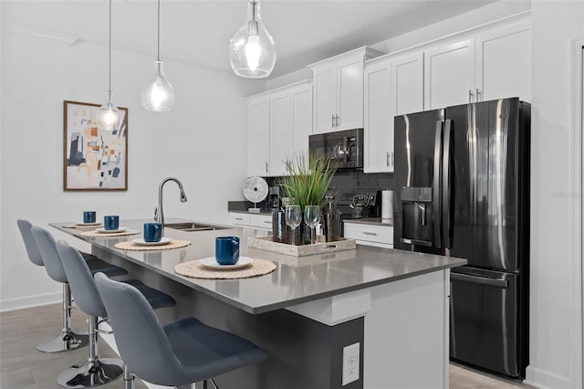 kitchen featuring refrigerator with ice dispenser, an island with sink, a sink, white cabinetry, and decorative backsplash