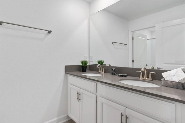 full bathroom featuring double vanity, baseboards, walk in shower, and a sink