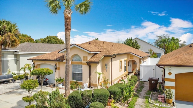 mediterranean / spanish-style house featuring roof with shingles, stucco siding, concrete driveway, a gate, and a garage