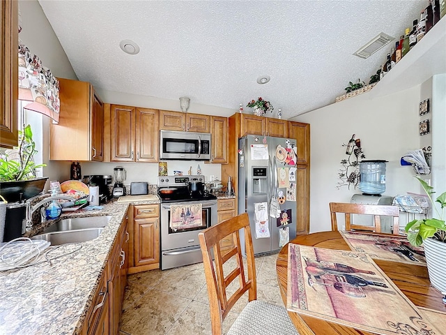 kitchen with appliances with stainless steel finishes, brown cabinets, visible vents, and a sink