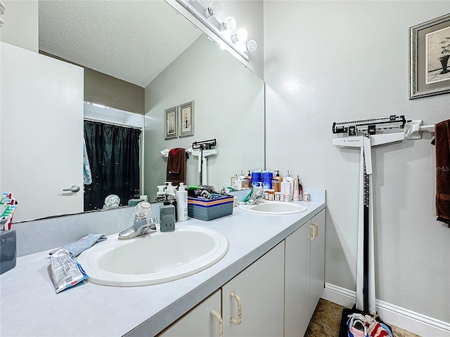 bathroom with a sink, a textured ceiling, baseboards, and double vanity