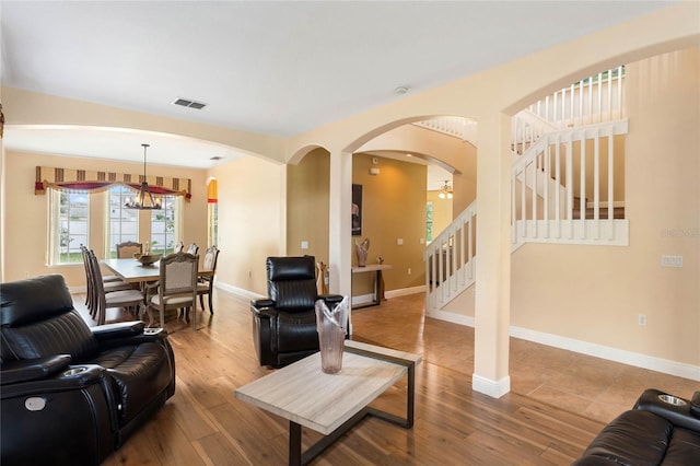 living room with baseboards, visible vents, wood finished floors, stairs, and a chandelier