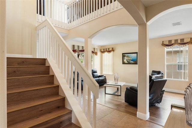 staircase with arched walkways, a towering ceiling, baseboards, and wood finished floors