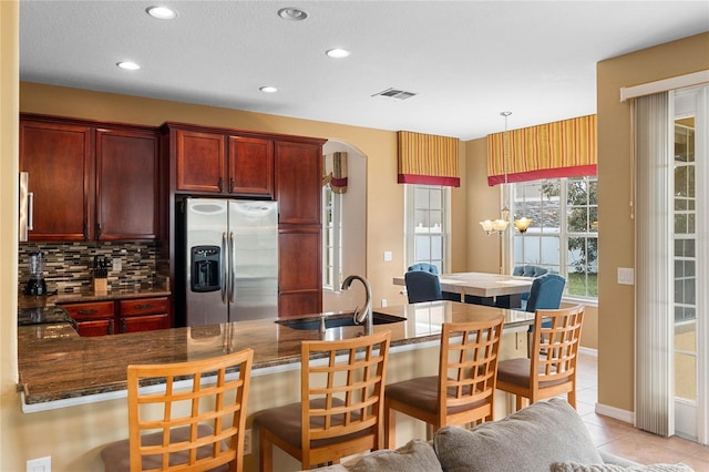 kitchen with a sink, visible vents, stainless steel fridge with ice dispenser, reddish brown cabinets, and tasteful backsplash