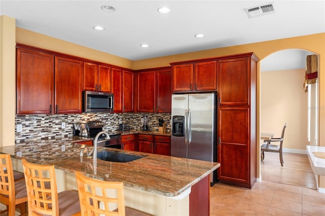 kitchen featuring a peninsula, visible vents, dark brown cabinets, appliances with stainless steel finishes, and dark stone countertops