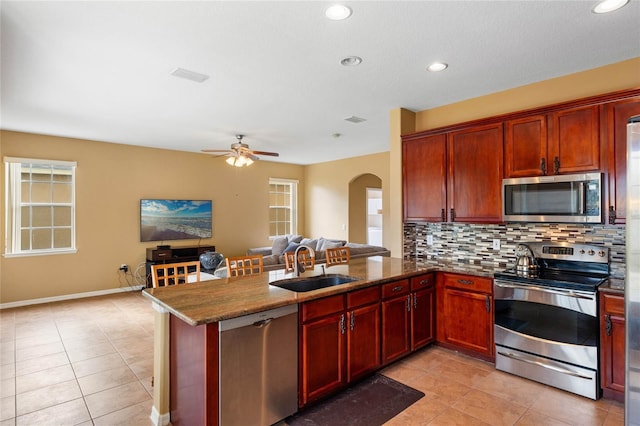 kitchen featuring arched walkways, stainless steel appliances, a sink, open floor plan, and decorative backsplash