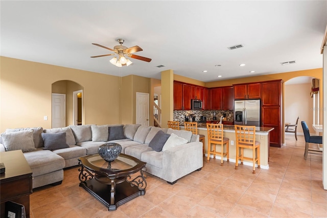 living area with visible vents, arched walkways, and ceiling fan