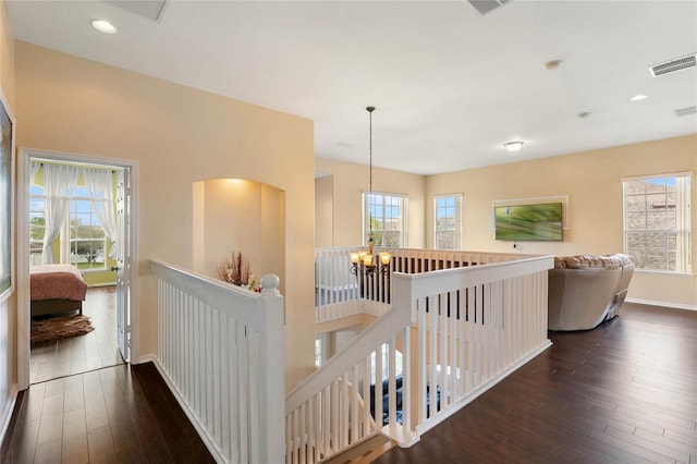 hallway featuring hardwood / wood-style flooring, baseboards, visible vents, and an upstairs landing