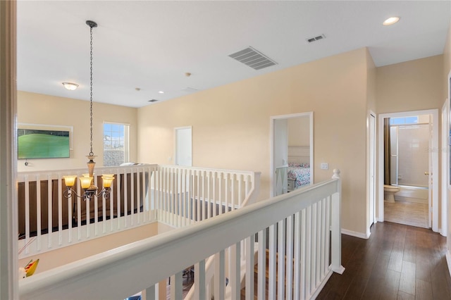 corridor with dark wood-type flooring, a chandelier, visible vents, and an upstairs landing