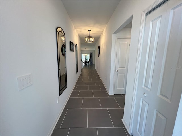 corridor featuring dark tile patterned floors, baseboards, and an inviting chandelier