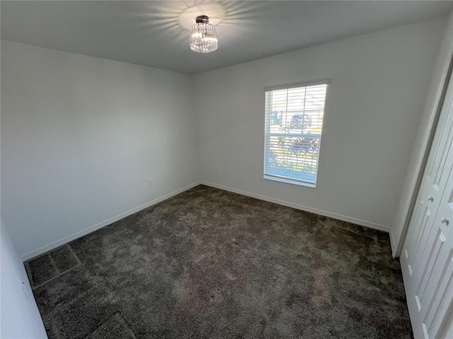 empty room with carpet, baseboards, and a notable chandelier