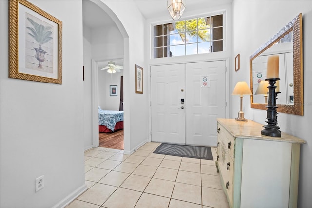 foyer entrance with light tile patterned floors, baseboards, arched walkways, and ceiling fan