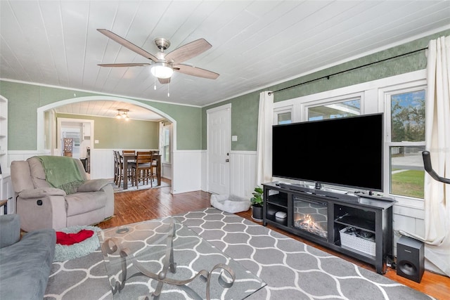 living room with arched walkways, wainscoting, crown molding, and wood finished floors