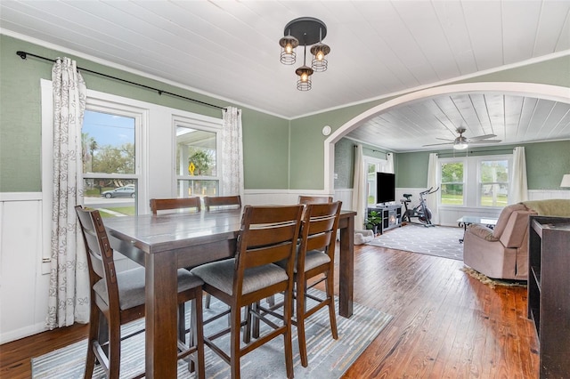 dining space with arched walkways, wainscoting, hardwood / wood-style flooring, wood ceiling, and ornamental molding