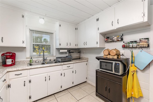 kitchen featuring light tile patterned floors, light countertops, stainless steel microwave, white cabinetry, and a sink