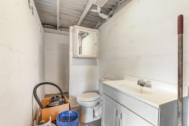 bathroom featuring concrete block wall, toilet, and vanity