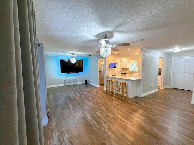 unfurnished living room featuring ceiling fan, a textured ceiling, wood finished floors, and baseboards