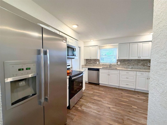 kitchen featuring stainless steel appliances, tasteful backsplash, white cabinetry, a sink, and wood finished floors