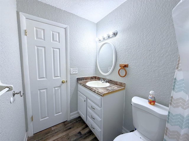 bathroom with toilet, a textured wall, wood finished floors, and vanity