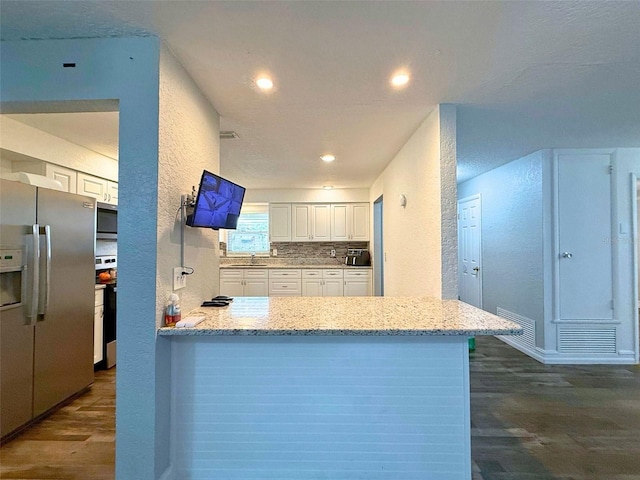 kitchen featuring white cabinets, a textured wall, light stone counters, dark wood-style flooring, and stainless steel appliances