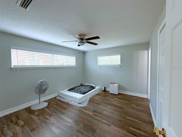 interior space with visible vents, a ceiling fan, a textured ceiling, wood finished floors, and baseboards