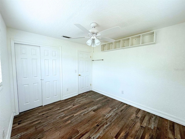 unfurnished bedroom with a textured ceiling, visible vents, baseboards, a closet, and dark wood finished floors