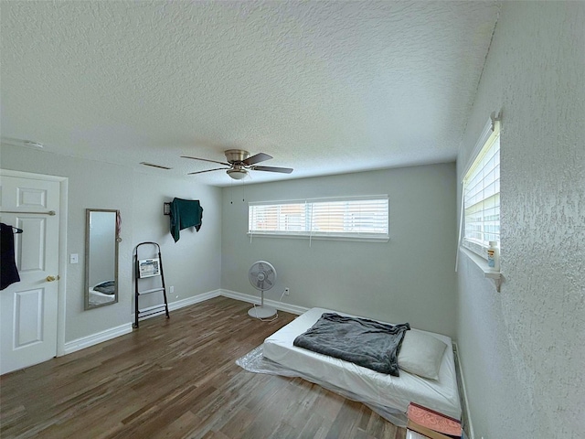 bedroom featuring visible vents, baseboards, a ceiling fan, wood finished floors, and a textured ceiling