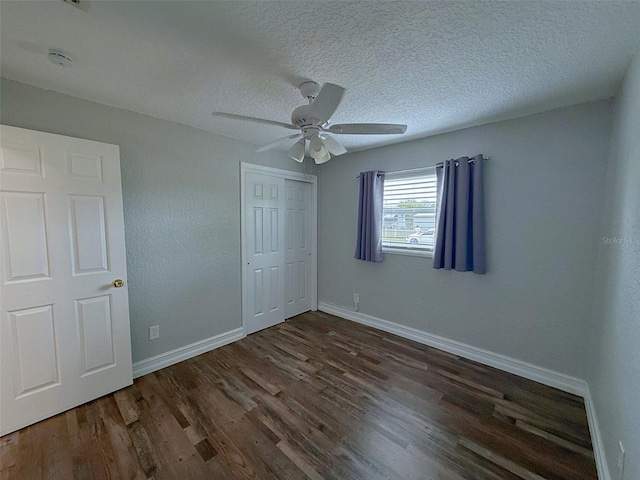 unfurnished bedroom with a closet, a ceiling fan, a textured ceiling, wood finished floors, and baseboards