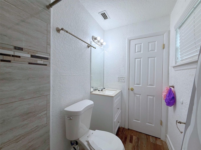 bathroom featuring visible vents, a textured wall, toilet, and wood finished floors