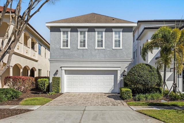 view of front of house with decorative driveway, an attached garage, and stucco siding