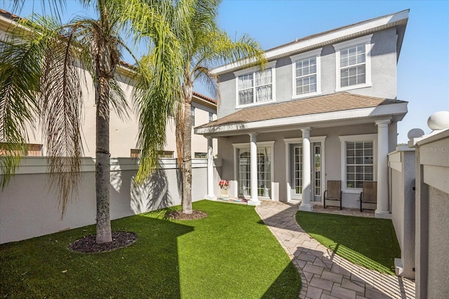 back of property featuring fence, a porch, roof with shingles, stucco siding, and a yard