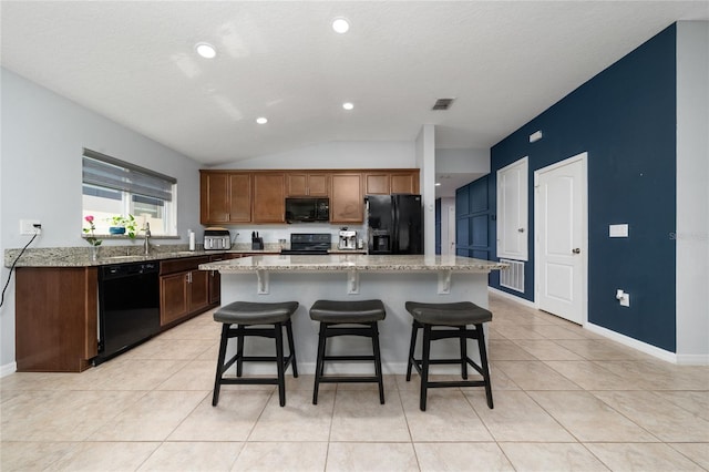 kitchen with light tile patterned floors, a breakfast bar, a kitchen island, visible vents, and black appliances